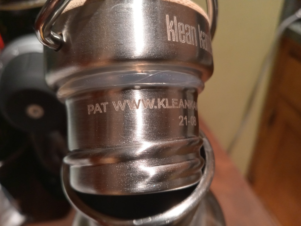 photo of reusable bottle cap product with "PAT WWW.KLEAN..." virtual patent marking notice etched into metal of the product